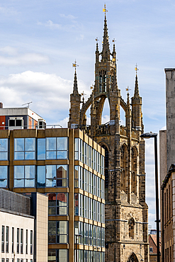 A Gothic tower with gold finials stands beside modern buildings featuring glass facades and concrete structures under a cloudy sky in Newcastle upon Tyne, UK.