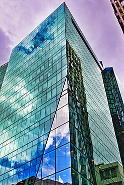 A modern glass building with a striking angular facade, reflecting a dramatic purple and blue sky with clouds in London, UK.