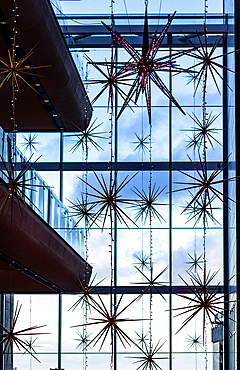 A modern interior features star-shaped decorations and string lights hanging against a large glass window with a cloudy sky view.