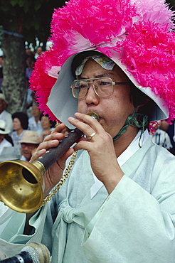 Portrait of a musician in a pink hat blowing an instrument during the Farmers Dance in Haewundae Park in Pusan City, South Korea, Asia