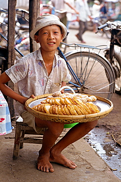 Portrait of a boy selling sweet cakes on the pavement in the town of Rach Gia in the Mekong Delta, Vietnam, Indochina, Southeast Asia, Asia