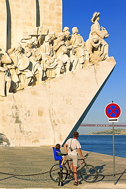 Father and son on a bicycle in front of the Monument of the Discoveries (Padrao dos Descobrimentos) inaugurated in 1960, by the Tejo River in Lisbon, Portugal, Europe