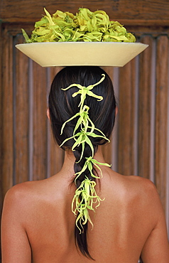 Back view of young woman with long hair balancing a bowl of ylang ylang on her head