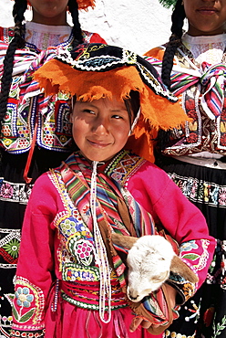 Portrait of a local smiling Peruvian girl in traditional dress, holding a young animal, Cuzco, Peru, South America