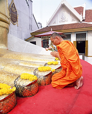 Buddhist monk kneeling and praying at the feet of a standing Buddha, Wat Intharawihan, Bangkok, Thailand, Southeast Asia, Asia