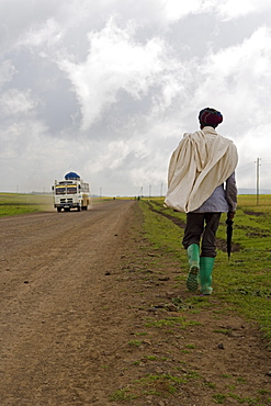 Man walking along the road during the rainy season wearing green boots and holding an umbrella, The Ethiopian Highlands, Ethiopia, Africa