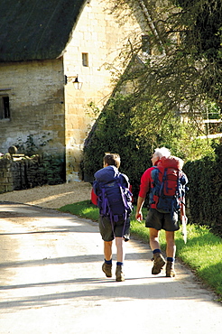 Two walkers with rucksacks on the Cotswold Way footpath, Stanton village, The Cotswolds, Gloucestershire, England, United Kingdom, Europe