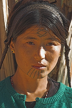 Naga (Macham tribe) girl with face tattoos, done when they are children so that they are not attractive to men who might steal them from their village) carrying wood on her back, Magyan Village, Sagaing Division, Myanmar (Burma), Asia