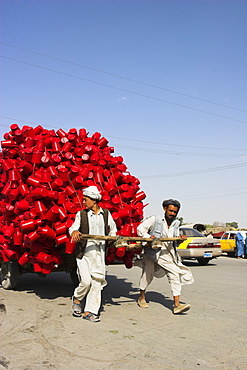 Men pulling wooden cart piled high with red water containers along road, Mazar-I-Sharif, Balkh province, Afghanistan, Asia