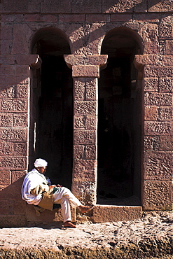 Pilgrim sits in early morning sun reading his Holy Bible at entrance doors to Bet Maryam church (St. Mary's), believed to be the oldest rock hewn church in Lalibela, UNESCO World Heritage Site, Lalibela, Ethiopia, Africa