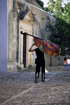 Musician carrying double bass along cobbled street to Plaza Mayor, Trinidad, Cuba, West Indies, Central America
