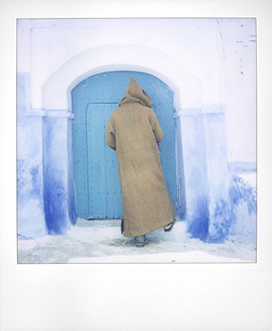 Polaroid of man wearing traditional woollen djellaba opening blue painted door to traditional house, Chefchaouen, Morocco, North Africa, Africa