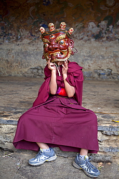 Young Buddhist monk holding traditional carved wooden mask to his face at the Tamshing Phala Choepa Tsechu, near Jakar, Bumthang, Bhutan, Asia