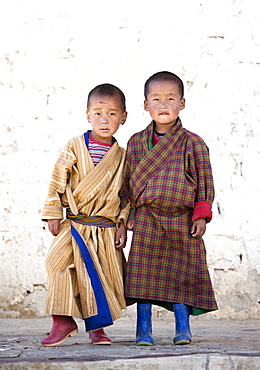 Two boys in front of white wall at Ura Lhakhang, Ura village, near Jakar, Bumthang, Bhutan, Asia