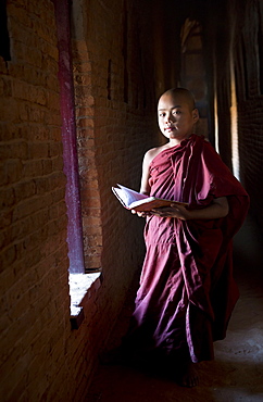 Novice Buddhist monk reading Buddhist scriptures in the light of a window in one of the many temples of Bagan, Myanmar (Burma), Asia