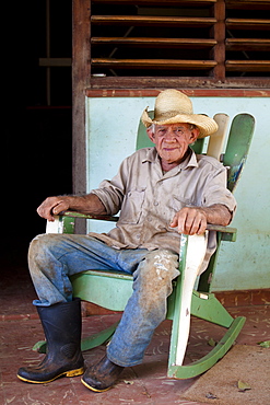 Tobacco farmer wearing straw hat and Wellington boots, on a rocking chair outside his house, Vinales, Pinar Del Rio, Cuba, West Indies, Central America