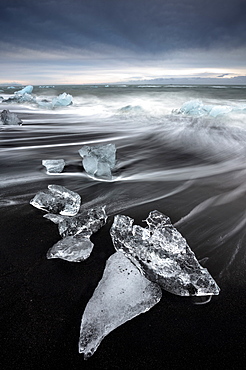 Glassy pieces of ice on volcanic black sand beach with blurred waves, near Jokulsarlon Lagoon, South Iceland, Polar Regions