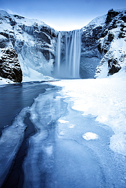 Winter view of Skogafoss waterfall, with cliffs covered in icicles and foregreound covered in snow, Skogar, South Iceland, Polar Regions