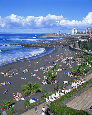 Tourists on volcanic sand beach at Playa Jardin, with San Felipe Castle and Hotel Puerto Playa beyond, at Puerto de la Cruz, Tenerife, Canary Islands, Spain, Atlantic, Europe