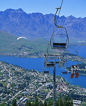 Tourists on a chair lift with Lake Wakatipu, the Remarkable Mountains and Queenstown, South Island, New Zealand, Pacific