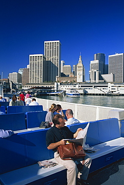 Man reading newspaper and passengers on the commuter ferry, with Ferry Building and skyline of downtown San Francisco in the background, California, United States of America, North America