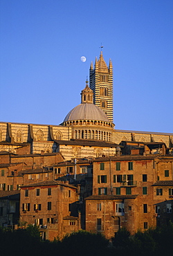 Moon in the sky above cathedral and houses clustered below at sunset, Siena, Tuscany, Italy, Europe