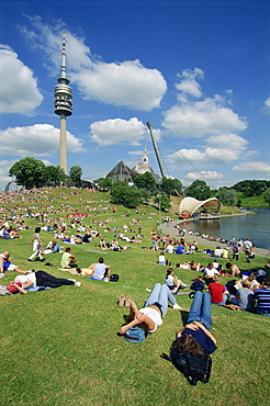 People relaxing on the grass in the Olympic Park with the Olympic Tower in the background, in Munich, Bavaria, Germany, Europe