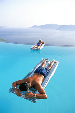 Holidaymakers on lilos in pool looking across bay, Oia, Santorini (Thira), Greek Islands, Greece, Europe