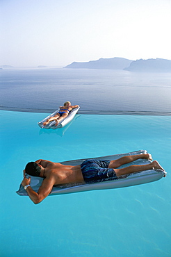 Holidaymakers on lilos in pool looking across bay, Oia, Santorini (Thira), Greek Islands, Greece, Europe