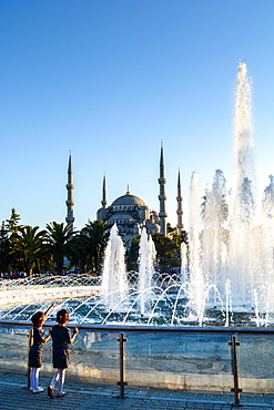 Two young Turkish girls pointing to the Blue Mosque, UNESCO World Heritage Site, with fountains in foreground, Istanbul, Turkey, Europe