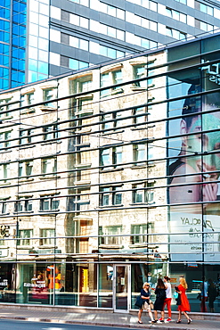 Building reflections with women in brightly coloured dresses on sidewalk near Galeria Riga, Riga, Latvia, Europe