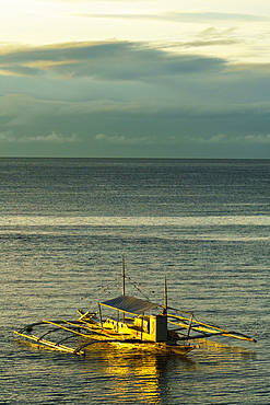 A lone bangka (outrigger canoe) bathed in warm dawn light berthed by Panglao Beach, Bohol Island, Philippines, Southeast Asia, Asia