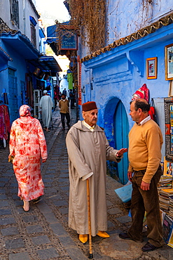 Street scene, old man with stick and red fez (hat) stops to talk with a the owner of a bookshop, Chefchaouen, Morocco, North Africa, Africa