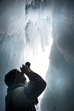 Tourist framed in the frozen mouth of ice cave, with icicles formed on roof of caves at Olkhon Island as the waves freeze in winter, Lake Baikal, Irkutsk Oblast, Siberia, Russia, Eurasia