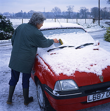 Woman scraping snow off the windscreen of a car in winter, United Kingdom, Europe