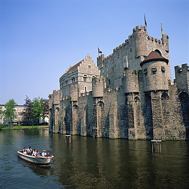 Small tourist boat passing the Castle of the Counts of Flanders in the city of Ghent, Belgium, Europe