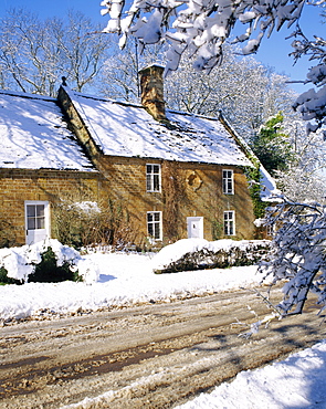 Cotswold farmhouse beside a road covered in snow in winter in England 