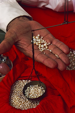 Close-up of hand displaying pearls with weighing scales, in the pearl souk, Manama, Bahrain, Middle East