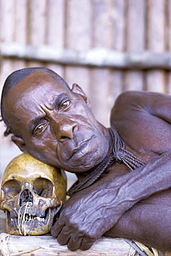 Portrait of an Asmat tribesman leaning on a human skull, Irian Jaya (West Irian) (Irian Barat), New Guinea, Indonesia, Asia