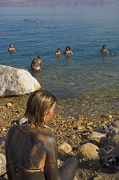 Woman's back covered with mud and people floating in the sea in background, Ein Gedi Beach, Dead Sea, Israel, Middle East