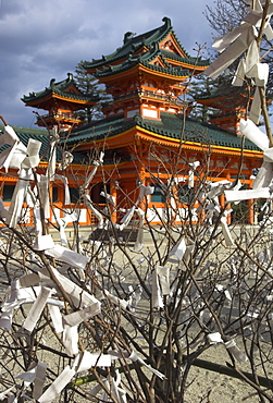 Fate and wish papers tied on a bush branches in foreground and temple beyond, Heian Jingu shrine, Kyoto, Kansai, Honshu, Japan, Asia