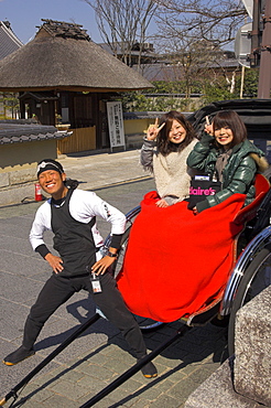 Rickshaw driver and two young Japanese women in rickshaw with red blanket waving at camera, Maruyama park, Higashiyama neighbourhood, Kyoto, Kansai, Honshu, Japan, Asia