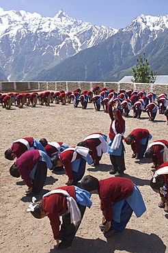 Group of school children in uniform during morning physical training in school courtyard with high snowy mountains in background, village of Kalpa, Recong Peo area, Kinnaur, Himachal Pradesh, India, Asia