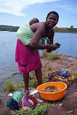 Baby sleeps on mother's back as she washes clothes, Uganda, East Africa, Africa