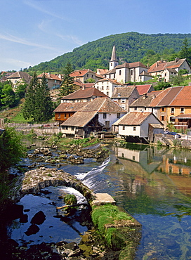 The weir and remains of a medieval bridge on the River Loue, with the houses and church of the village of Lods in Franche-Comte, France, Europe