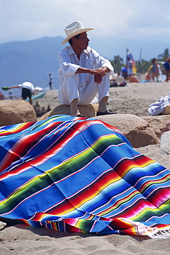 A man selling striped woven blankets or rugs in vibrant primary colours on the beach at Puerto Vallarta, Mexico, North America