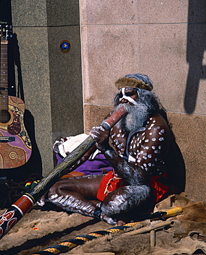 Portrait of an Aboriginal man with traditional facial and body paint, playing a digeridoo, busking in the street, in Sydney, New South Wales, Australia, Pacific