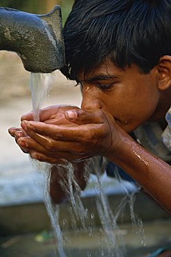 Close-up portrait of a Bangladeshi boy cupping his hands and drinking water from a bore hole in Bangladesh, Asia