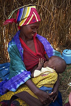 Portrait of a Rwandan refugee woman in traditional clothing, sitting on the ground breastfeeding her baby, Tanzania, East Africa, Africa