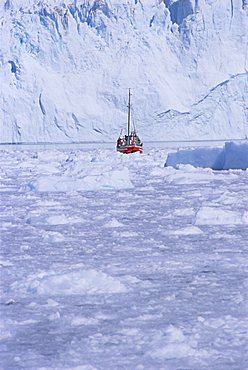 Red wooden boat crossing the ice in front of the Eqi Glacier, near Ilulissat, Greenland, Polar Regions